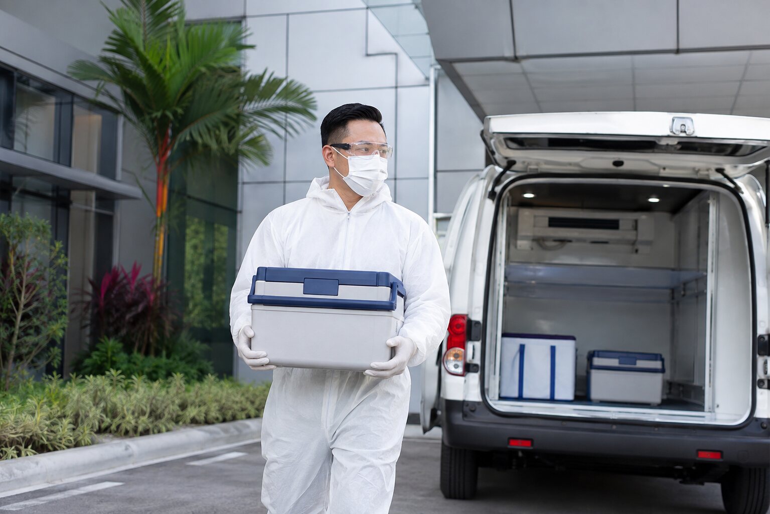 Protective-suited healthcare logistics worker carrying a sealed medical transport cooler